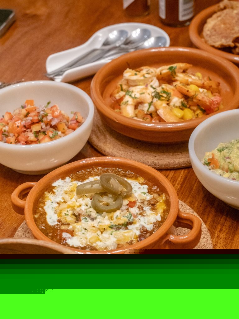 Food spread with gambas, chili con carne, pico de gallo, and guacamole